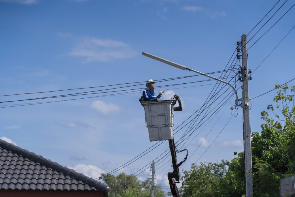 Electrician standing in the basket of a car fixing a lamp at a power pole